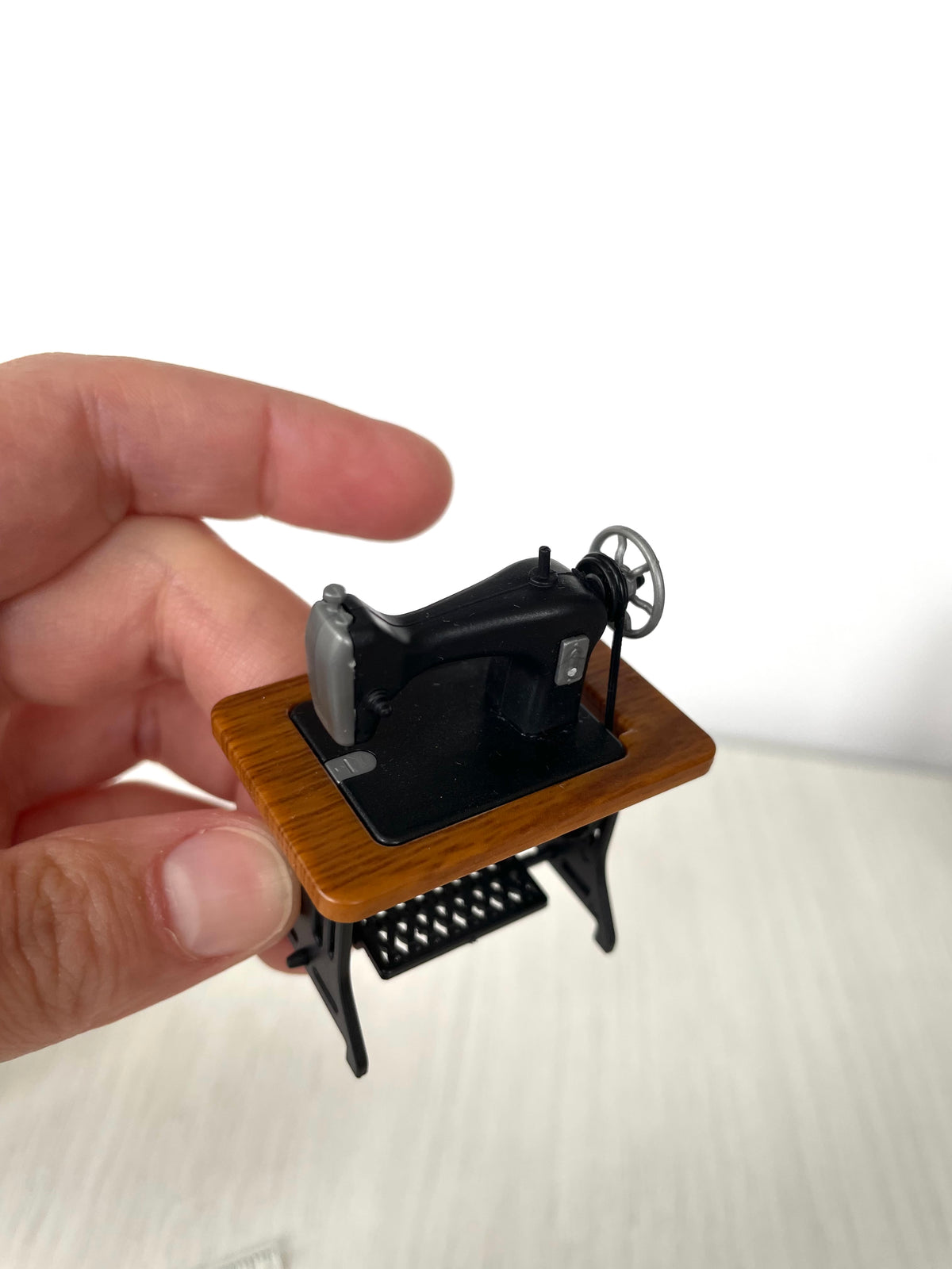 Vintage treadle sewing machine held in hand, three-quarter front angle — Calico Critters and Sylvanian Families