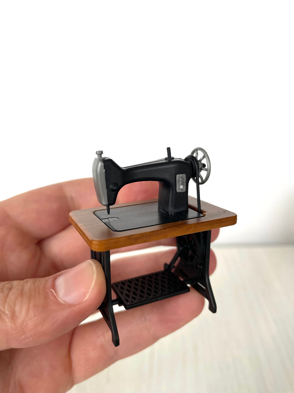 Vintage treadle sewing machine held in hand, front angle showing the spoked wheel — Calico Critters and Sylvanian Families