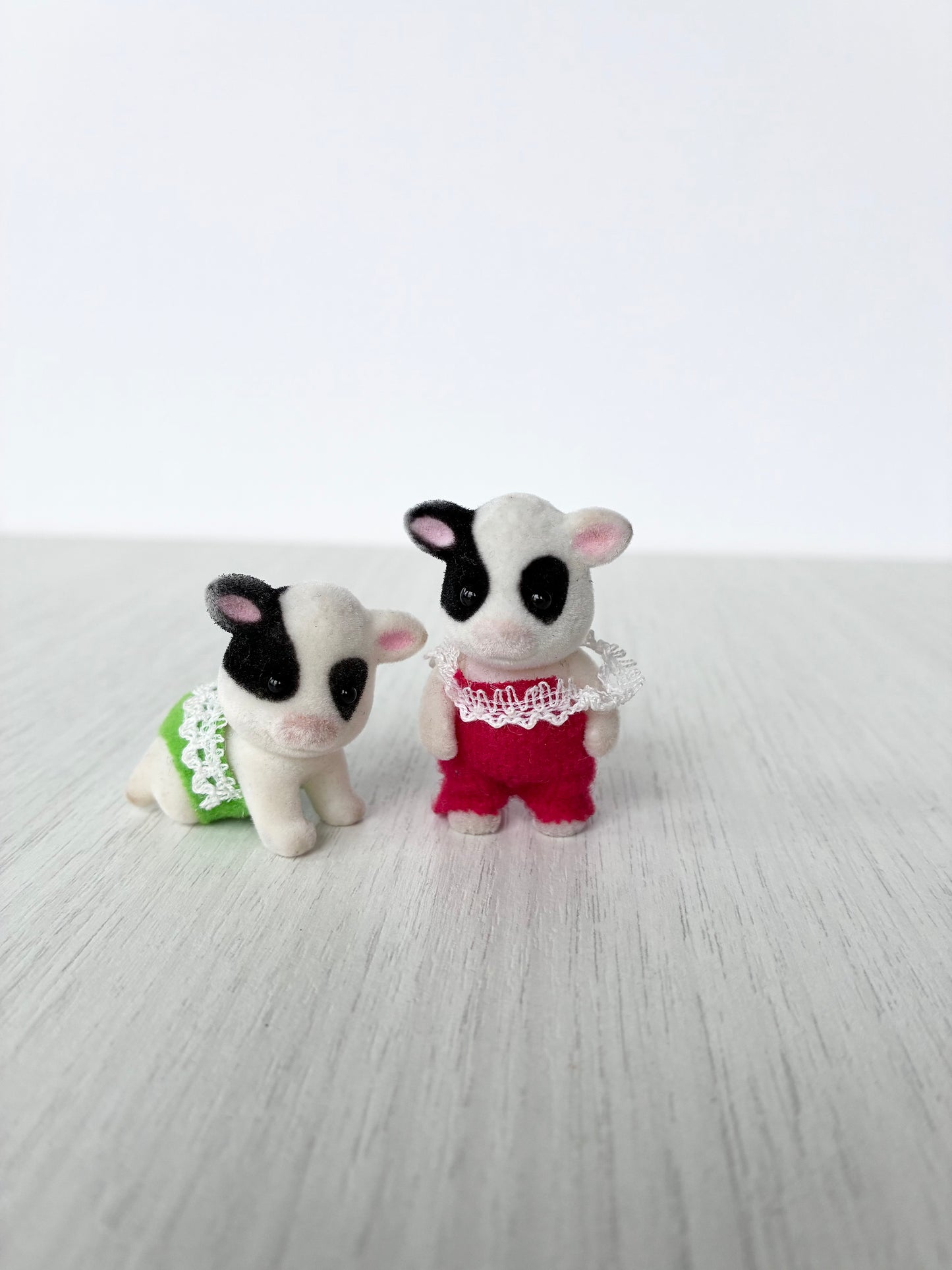 Calico Critters Sylvanian Families Buttercup Friesian cow baby twins side by side, one standing on articulated legs in red and one in crawling pose in green