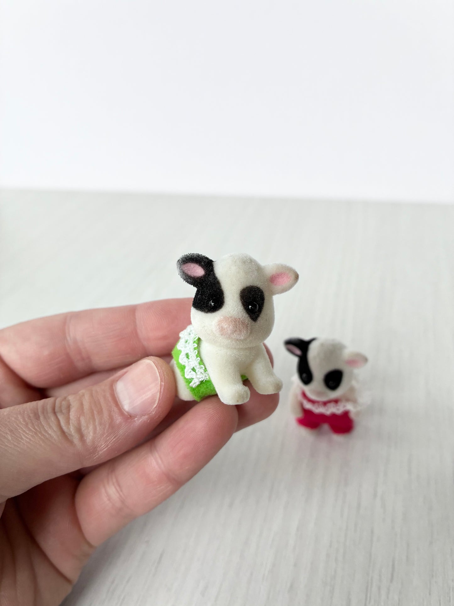 Calico Critters Sylvanian Families Friesian cow baby figures, front view showing crawling pose calf in green and standing articulated calf in red