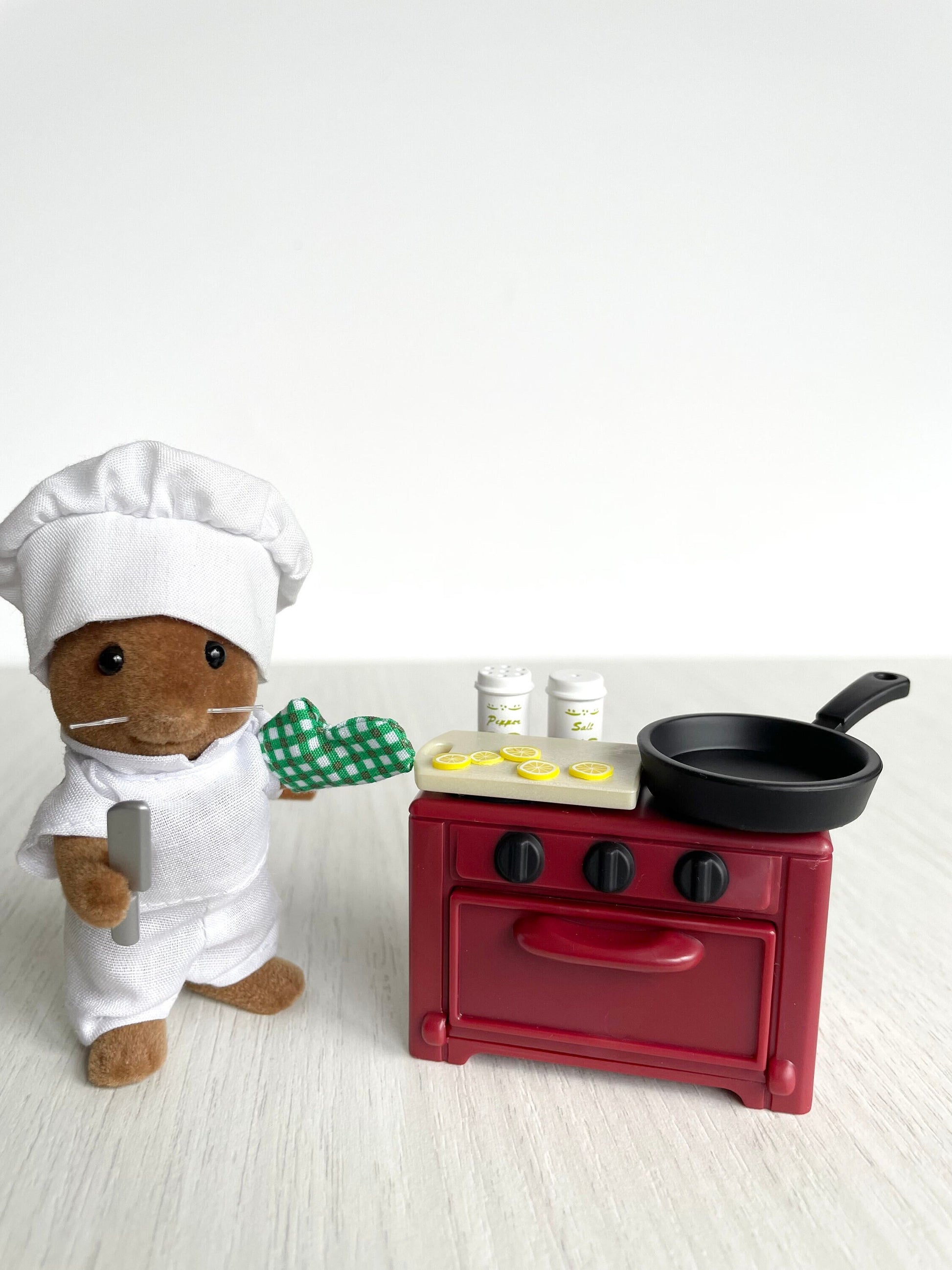 Miniature chef mouse figure with dollhouse kitchen cooking stove and frying pan with cutting board, oven mitts, salt & pepper shaker + lemon. This set comes with basil holding his knife and wearing his chef outfit slicing lemons.