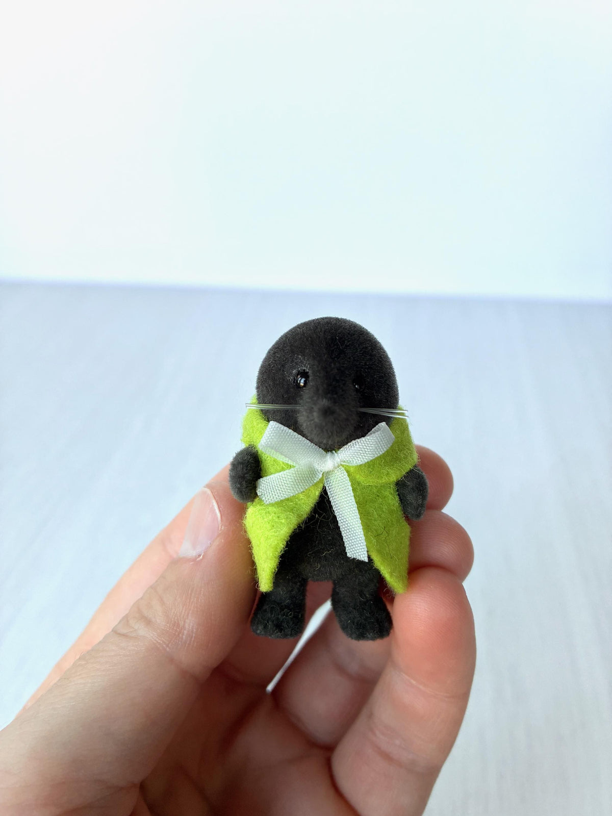 Calico Critters Sylvanian Families vintage McBurrows mole family, child mole in a green felt cape with white ribbon, held in hand for scale
