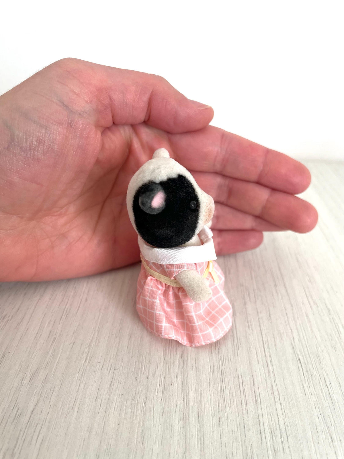 Overhead view of the cow girl held in hand showing her black and white patched head and pink dress — Calico Critters and Sylvanian Families