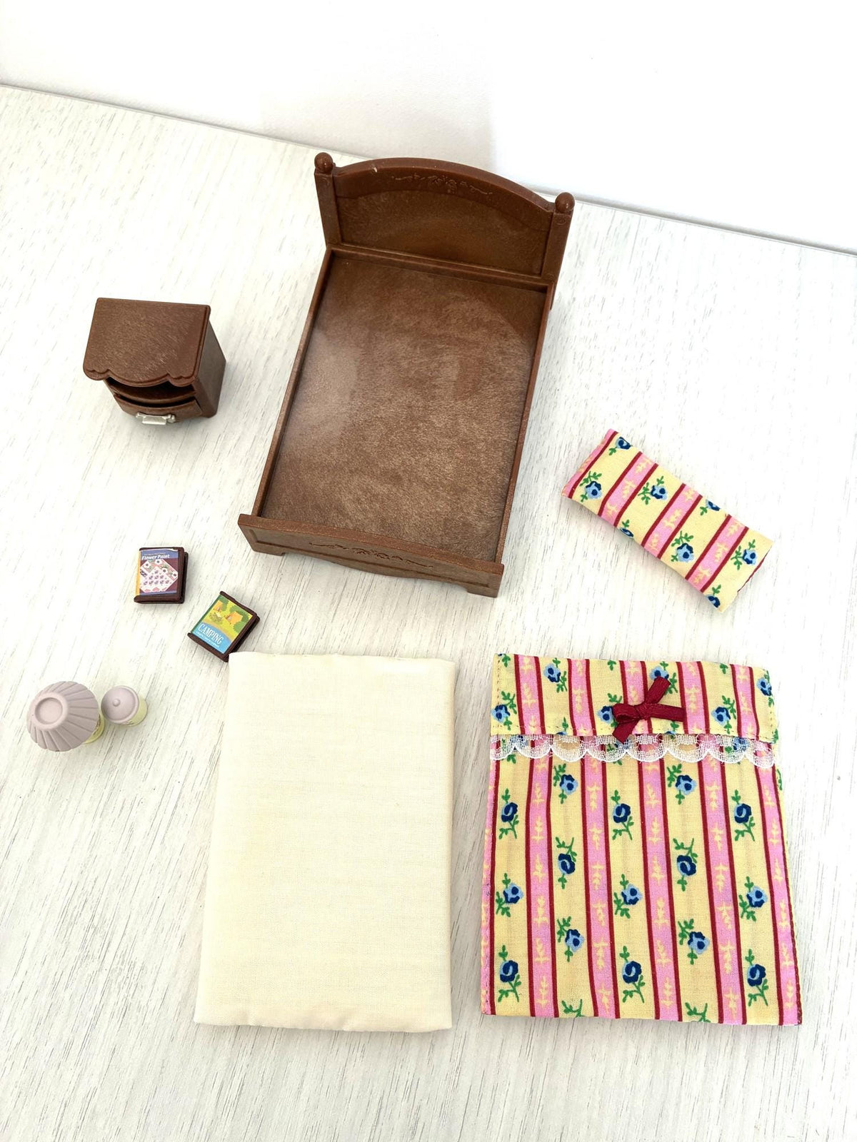 Calico Critters Sylvanian Families bedroom set laid out, bed frame, mattress, quilt, pillow, table, lamp and books