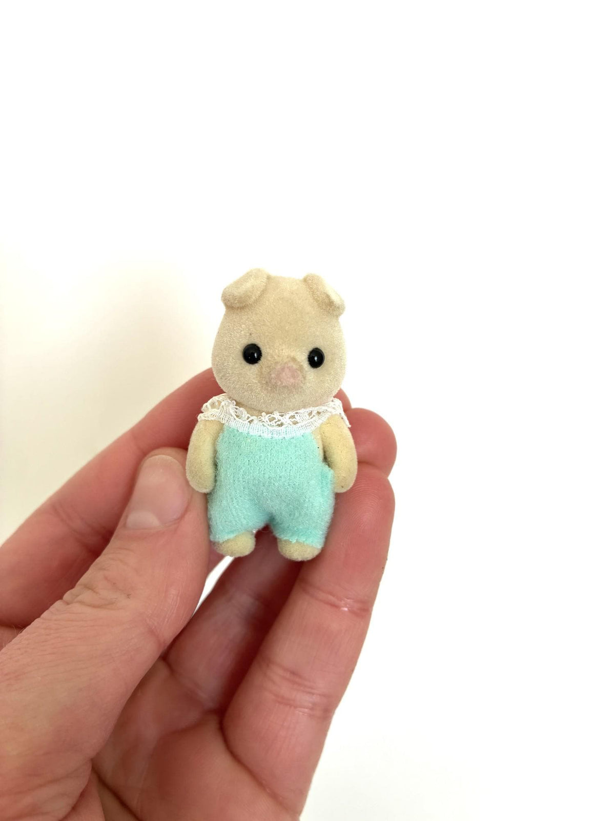 Calico Critters Sylvanian Families cream pig baby in mint green romper, standing jointed baby, front view held in hand