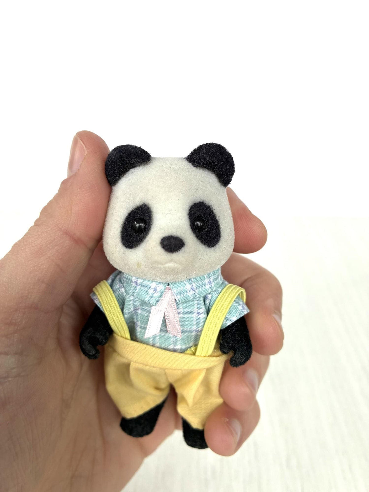 Calico Critters Sylvanian Families panda boy in blue check shirt and yellow dungarees, front view held in hand