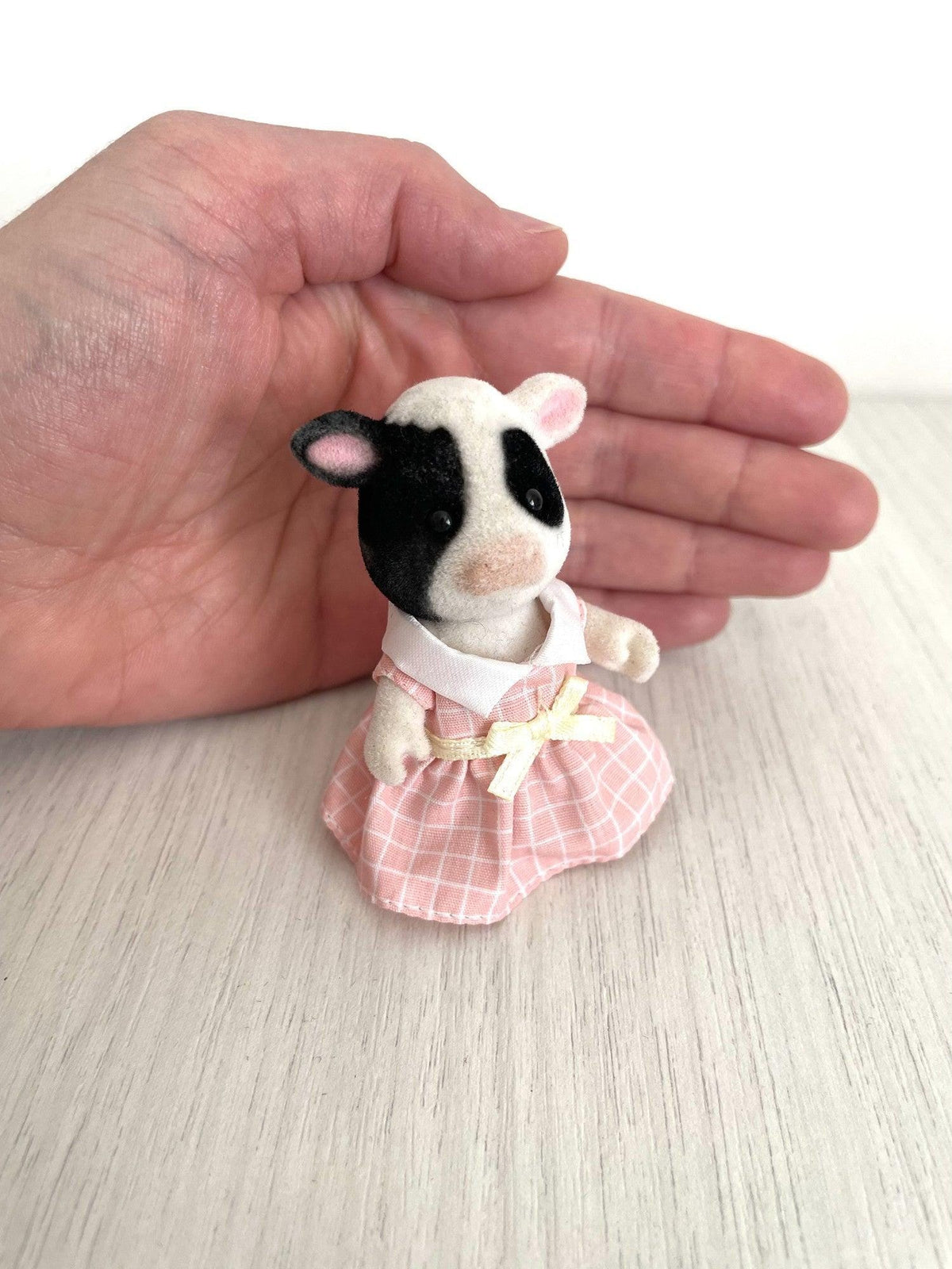 Cow girl held in hand for scale showing her black patch and pink ears — Calico Critters and Sylvanian Families