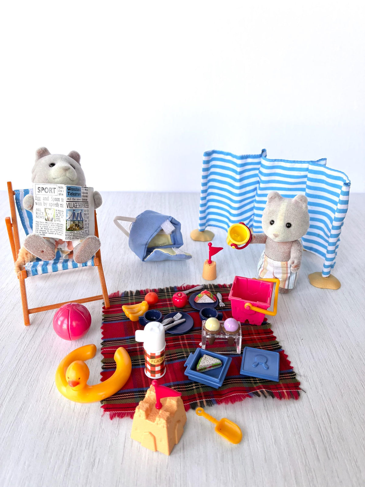 Sylvanian Families Calico Critters Day at the Seaside Set (Flair 4870): Harley Farthing dog reading the paper in a striped deck chair while Vespa holds a bucket by the tartan picnic rug, windbreak behind