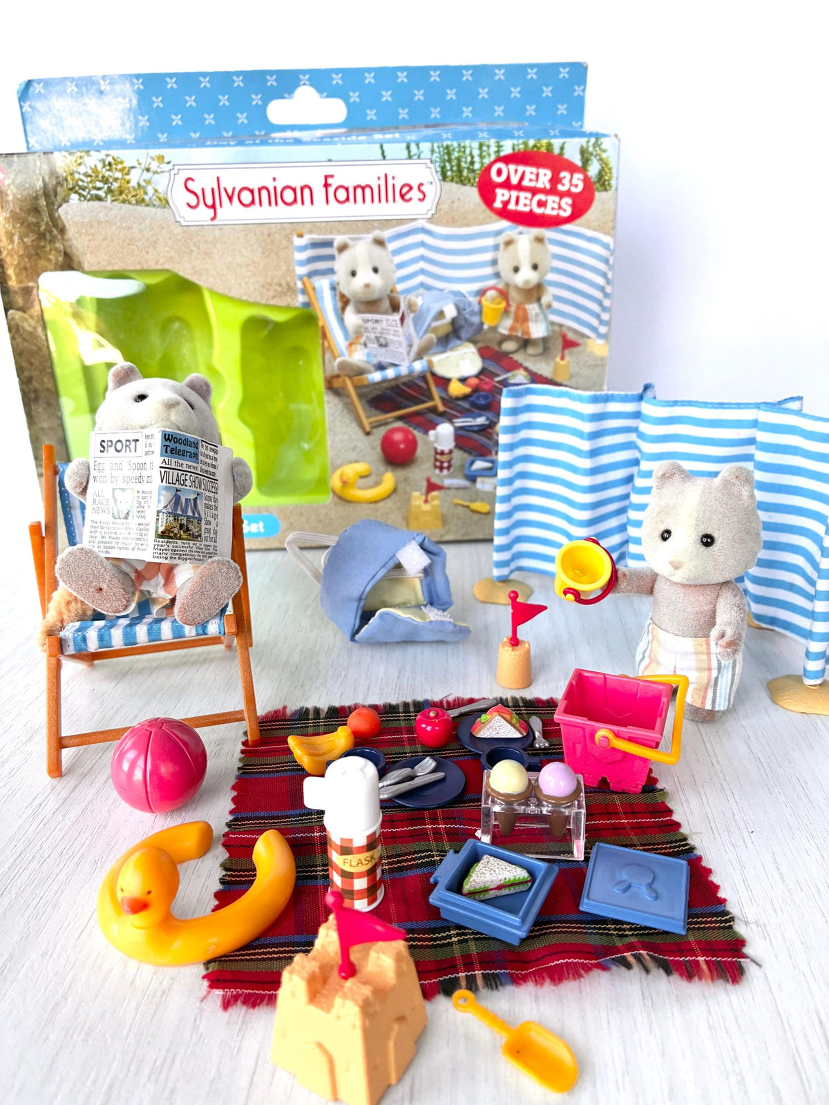 Sylvanian Families Calico Critters Day at the Seaside Set (Flair 4870): beach scene angled view with sandcastle, spade, duck ring and ball in front of the original Flair box