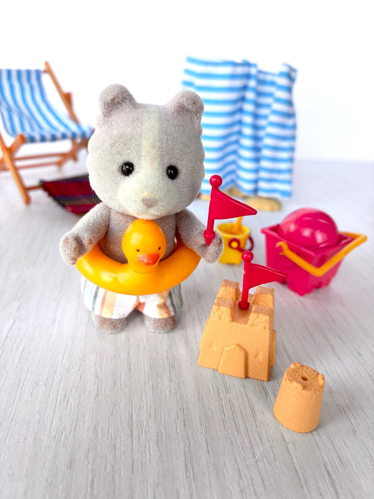 Sylvanian Families Calico Critters Day at the Seaside Set (Flair 4870): Vespa Farthing wearing the yellow duck rubber ring beside the sandcastle, sand pie and red bucket