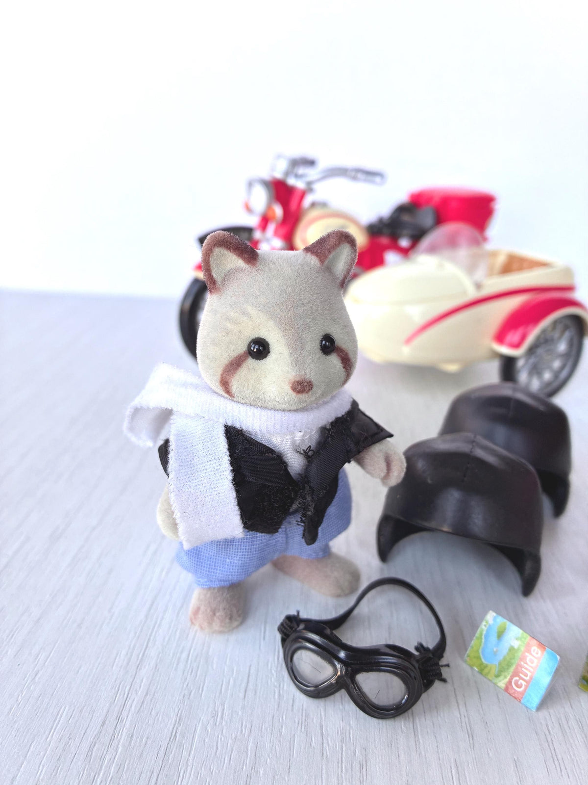 Calico Critters Sylvanian Families George Mulberry Raccoon Grandfather in white scarf, black vest and blue trousers with goggles and village guide, motorcycle behind him